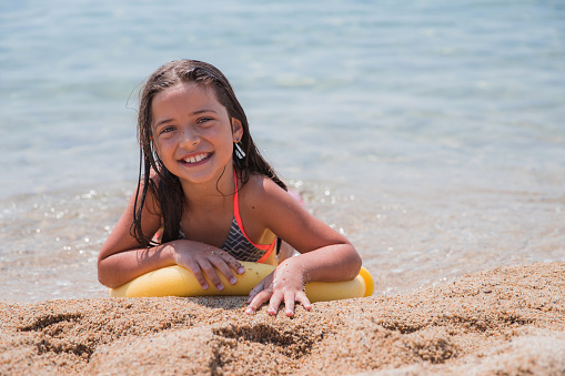 Beautiful teenage girl smiling when relaxing, lying on a woggle on the beach