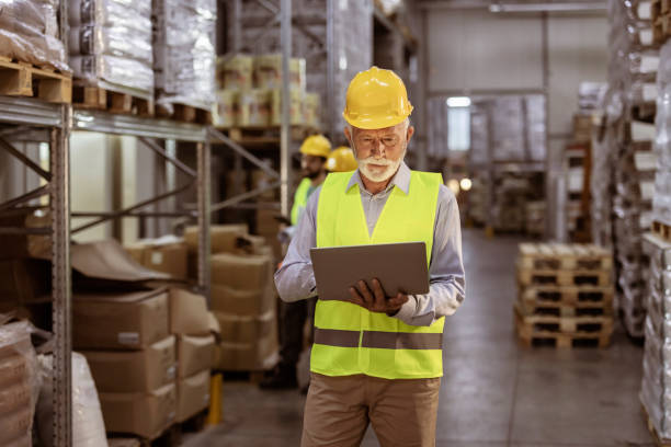 istock Senior Male Supervisor with Laptop in Warehouse 1385975820