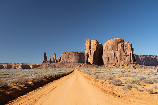 A dirt road straight into distant classic southwest desert landscape in Monument Valley in Utah and Arizona.