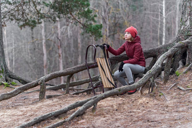 une fille vêtue d’une veste rouge et d’un chapeau est assise avec un traîneau sur une montagne dans la forêt - apres ski snow mountain loneliness photos et images de collection