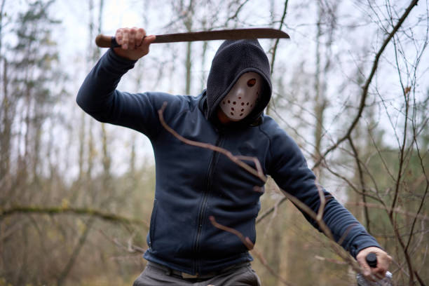 Serial killer Jason Voorhees in hockey mask and machete staying n the swamp Serial killer Jason Voorhees in hockey mask and machete staying n the swamp in the autumn forest. Friday 13h cosplay costume. jason machete stock pictures, royalty-free photos & images