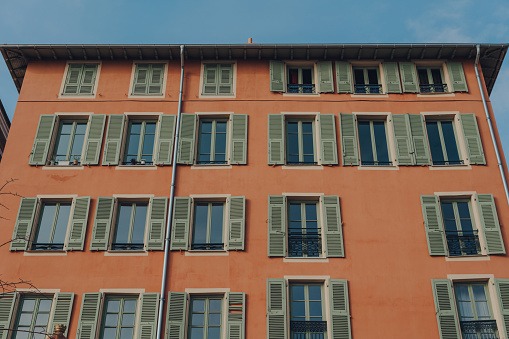 Low angle view of a traditional colourful apartment block building with shutters on windows in Nice, France.