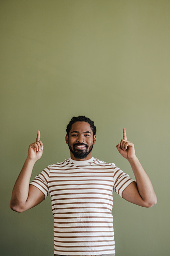 Studio shot of African American man with both index fingers up. He is standing against green wall.