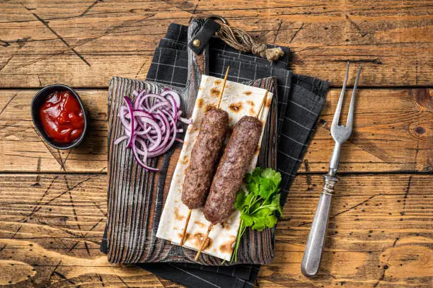 Traditional middle east kefta, kofta kebab from ground beef and lamb meat grilled on skewers served with flatbread and onion. Wooden background. Top view.