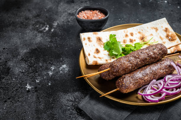 Lamb meat kofta kebab, onion and flat bread on plate. Black background. Top view. Copy space