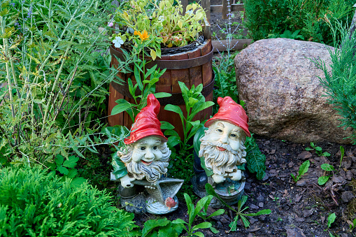 Small gnomes in red caps stand near an old wooden barrel