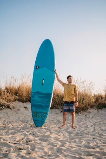 Man standing at beach leaning a blue paddleboard