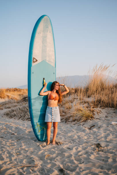Woman standing next to a paddleboard and looking into distance