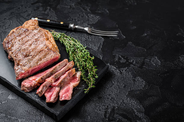 istock Griiled on BBQ sliced Striploin marbled beef meat steak. Black background. Top view. Copy space 1385983598