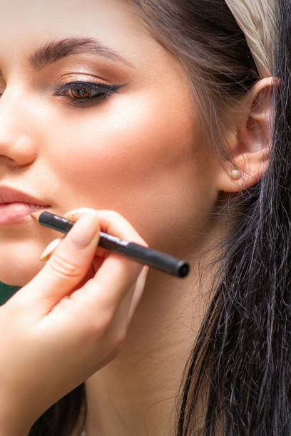 el maquillador profesional o cosmetólogo está pintando los labios de contorno de una mujer joven con un lápiz de cerca. - lip liner fotografías e imágenes de stock