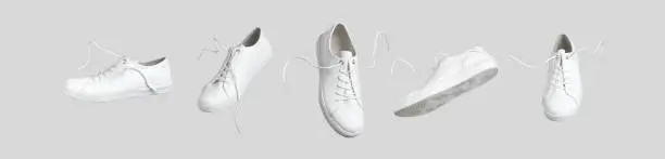 Photo of Flying white leather womens sneakers isolated on gray background, different kind. Fashionable stylish sports casual shoes. Creative minimalistic layout with footwear. Advertising for shoe store, blog