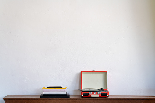 Pile of books and a retro turntable on a wooden shelf against a white wall. Record player. High quality photo