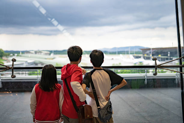 Rear view Asian Chinese siblings looking through window from the airport. stock photo