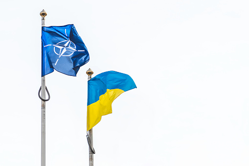 Kiev, Ukraine - March 3 2022: Flag of NATO, North Atlantic Treaty Organization and Ukraine waving together in the white sky, copy space