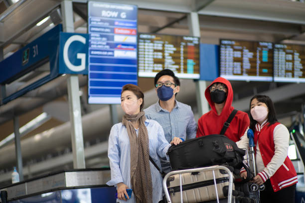 Asian Chinese family travelling by plane on a vacation, wearing mask, walking in airport concourse with luggage stock photo
