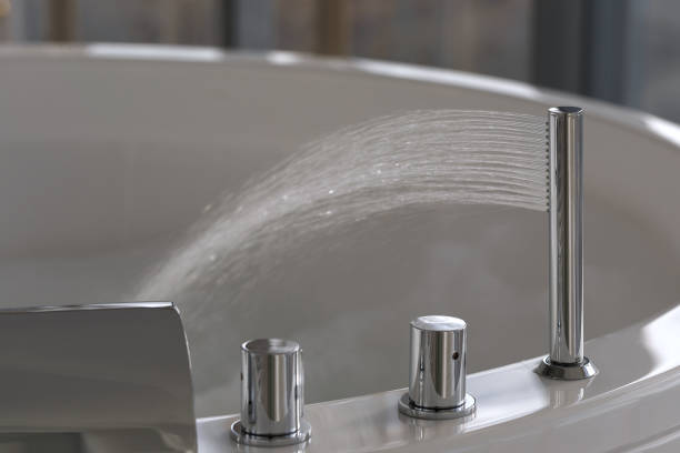 istock Water flows from a luxurious modern water faucet into a large modern bathtub. Spa, relaxation, hygiene concept 1385994635