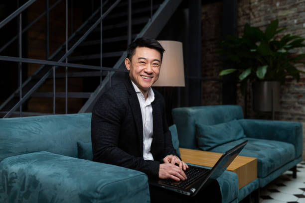 успешный азиатский бизнесмен, в черном деловом костюме, работает на ноутбуке, отдыхает в ресторане или отеле, а в стильном офисе объясняет н - asian ethnicity suit business men стоковые фото и изображения