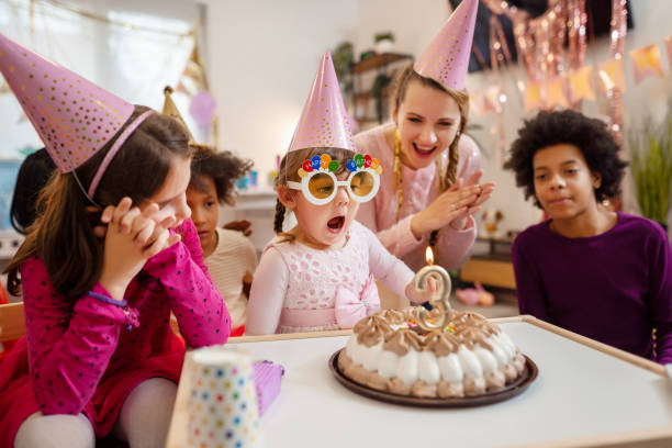 kleines mädchen, das seine geburtstagskerze bläst - spielzimmer fotos stock-fotos und bilder