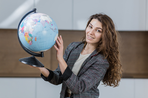 Portrait of young beautiful woman, travel agent, holding globe, looking at camera, smiling