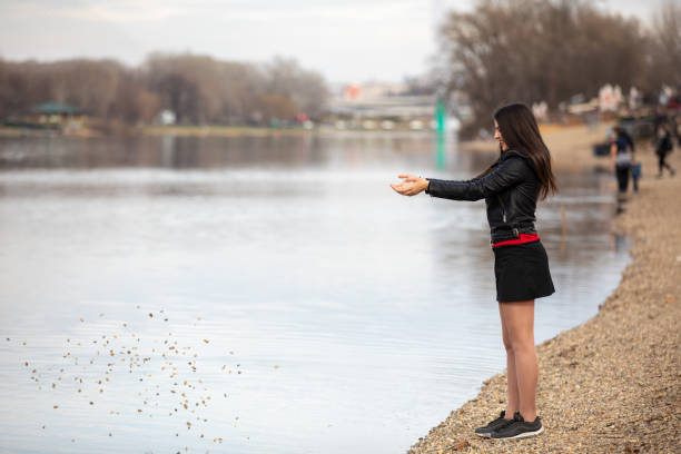 glückliches teenager-mädchen, das in der nähe des sees spielt. teenager wirft kieselsteine in den see. - throwing stone human hand rock stock-fotos und bilder