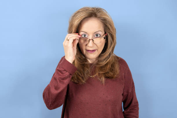 istock Woman looking over glasses with a surprised face, blue studio background. 1386009846