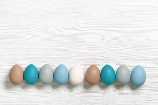 istock Easter eggs pastel colors lined up row on white wooden background with copy space. Easter celebration concept, card with dyed chicken egg beige, blue, gray colored. Top view holiday food 1386010086