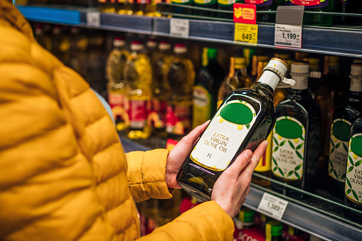 Woman buying olive oil from supermarket.. She's choosing from the shelf
