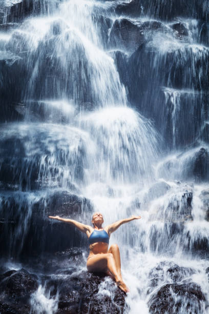 istock Woman sit on rock under cascade waterfall 1386016230