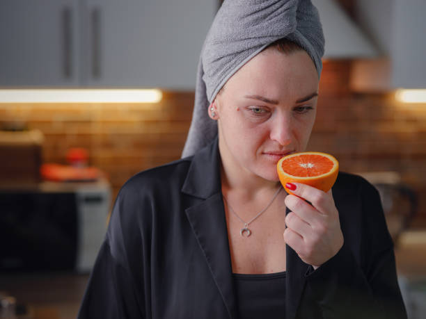 Sick woman trying to sense smell of fresh orange Sick woman trying to sense smell of fresh orange, has symptoms of Covid-19, corona virus infection. Long-lasting covid19 symptom. Loss of taste of food. Loss of smell as one of long-term sars-cov-2 effects. long covid stock pictures, royalty-free photos & images