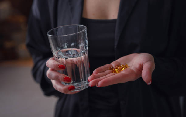 Woman in black shirt hold in hands pill omega 3 Woman hold in hands pill omega 3, vitamin D and glass of water, capsules with green vegan food. Taking minerals for female skin and health, prevention treatment, healthcare, skincare bodycare concept folic acid stock pictures, royalty-free photos & images