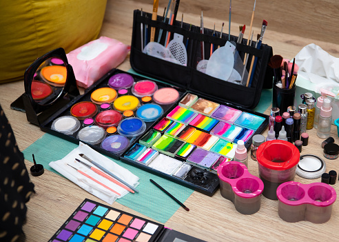 Colourful paint boxes and tubes with paints on a table. Paints and brushes for make-up, for painting on faces, face painting, face art. Abstract background and texture.