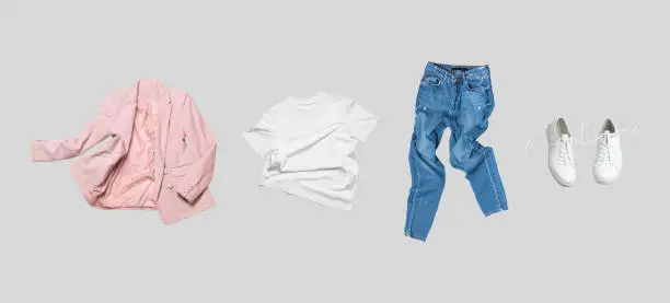 White flying cotton T-shirt, blue jeans, white leather sneakers, fashionable pink blazer jacket isolated on gray background. Clean Branding clothes. Mock up for your design. Spring Summer Clothing.