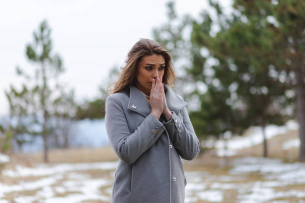 istock Young beautiful woman wearing a grey coat blowing into her hands because she is cold 1386033957
