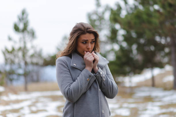 istock Young beautiful woman wearing a grey coat blowing into her hands because she is cold 1386033993