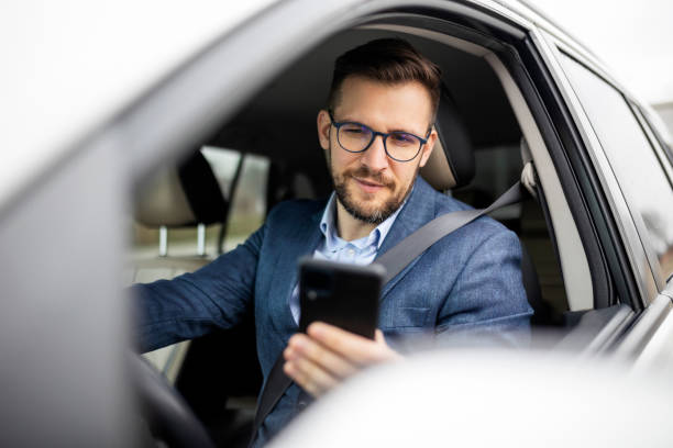 бизнесмен переписывается и ездит в своей машине - mobile phone seat belt text messaging smiling стоковые фото и изображения