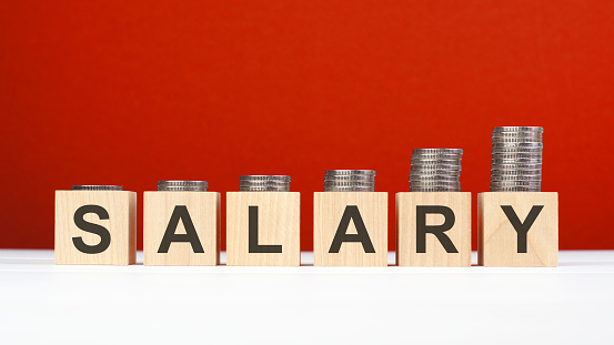 salary word made with wooden blocks with stacked coins. growing trend, red background.