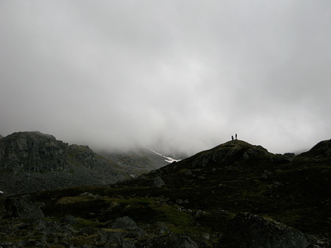 Two hikers pause in the midst of fog on a rocky ridge in Alaskan wilderness.