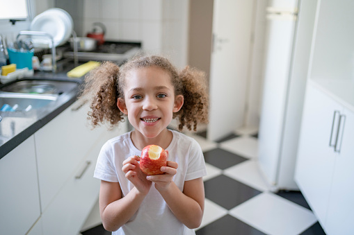 Little girl eating fruit in the kitchen at home