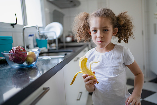 Little girl eating fruit in the kitchen at home
