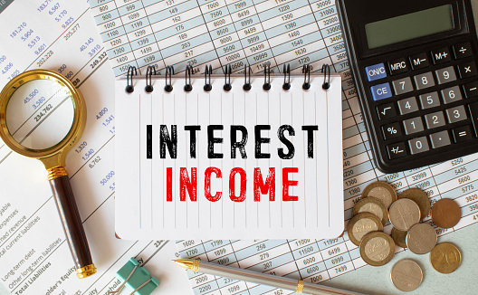 On a light background - reports, a magnifying glass, brown and red notepads, and a white notepad with the text INTEREST INCOME. Business concept