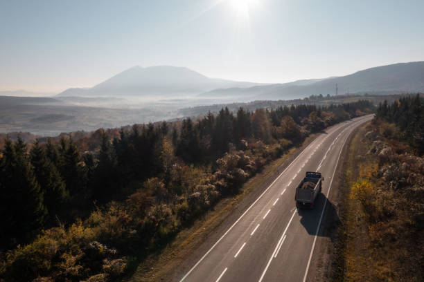 Aerial view of a highway with truck passing by and mountains in distance on a sunny day.