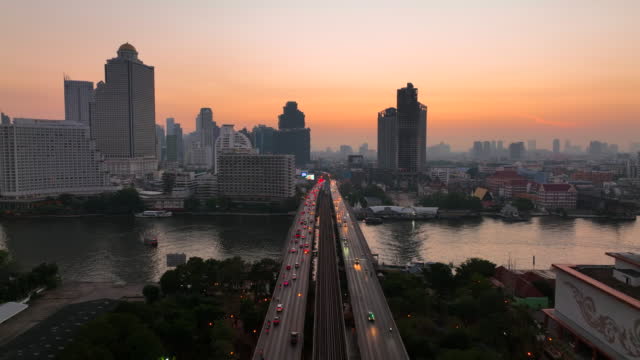 Aerial Drone Sunrise Scene of Traffic Car Light on Highway and  Metro Sky Train Across Chao Phaya River at Bangkok