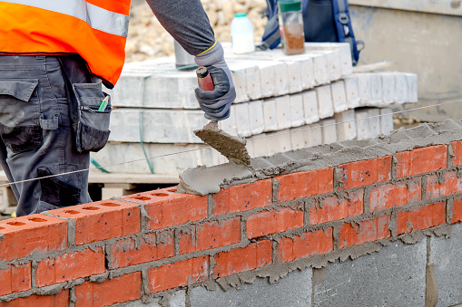 Bricklayer laying bricks on mortar on new residential house construction site