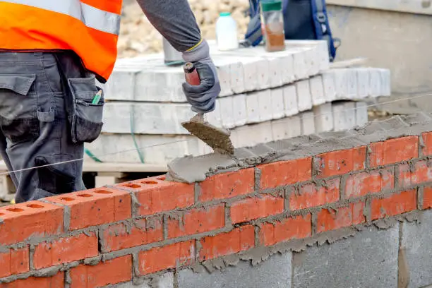 Photo of Bricklayer laying bricks on mortar on new residential house construction