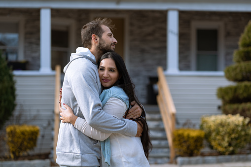 Adult brother and sister hugging in front of their house