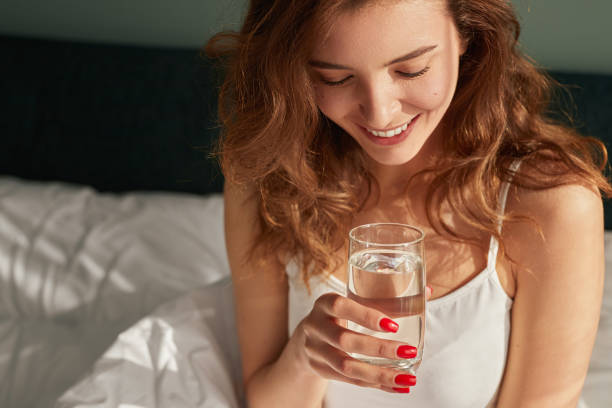 istock Cheerful young female drinking water on bed 1386079397