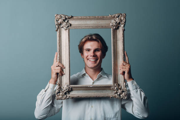 Portrait young man standing with picture frame at studio. stock photo