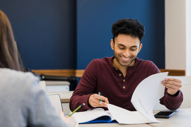 Young adult students enjoy studying together The young adult man smiles as he and his unrecognizable female friend study together. mediterranean ethnicity stock pictures, royalty-free photos & images