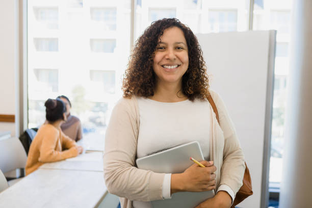 Non-traditional female college student holding laptop smiles for camera Standing in the college classroom, the non-traditional students holds her laptop as she smiles for the camera. iberian ethnicity stock pictures, royalty-free photos & images