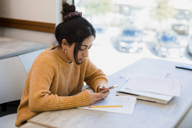 Young woman uses phone to find answers for test The young adult woman uses her smart phone to surf the net for the answers to her test. midwestern state university stock pictures, royalty-free photos & images